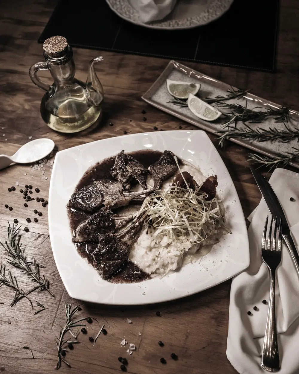Assiette dressée sur une table de bois sombre, huile et romarin en second plan